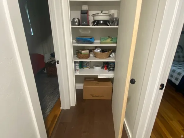 Pantry closet with multiple shelving units and wood-finish flooring