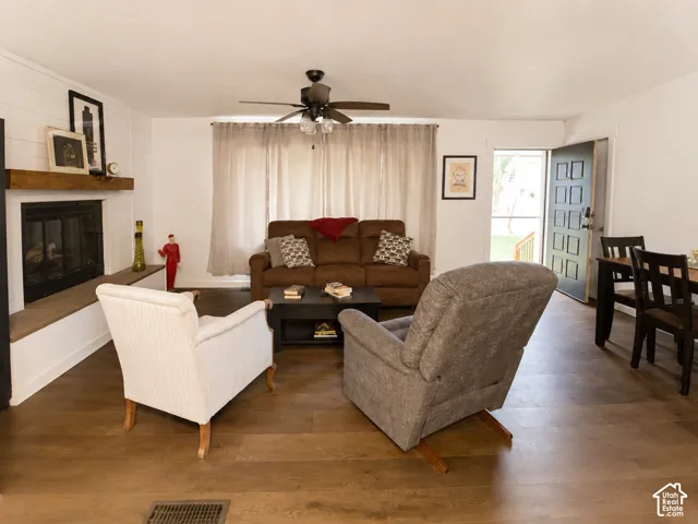Fireplace with a wood mantel, wood-finish flooring, shiplap accent wall, and ceiling fan with integrated lighting