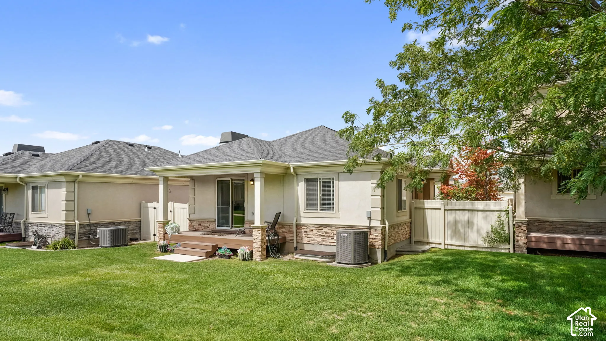 Expansive grass lawn with a covered patio featuring stone-clad pillars, sliding glass door access, and a wood-finish deck