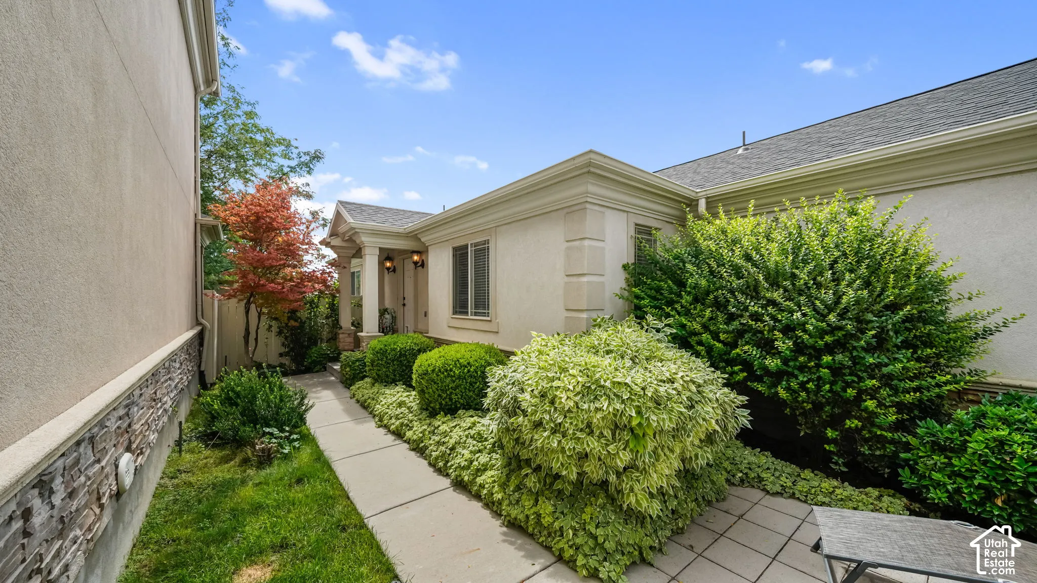 Stucco exterior with stone accent, concrete walkway, mature shrubs, and covered entry