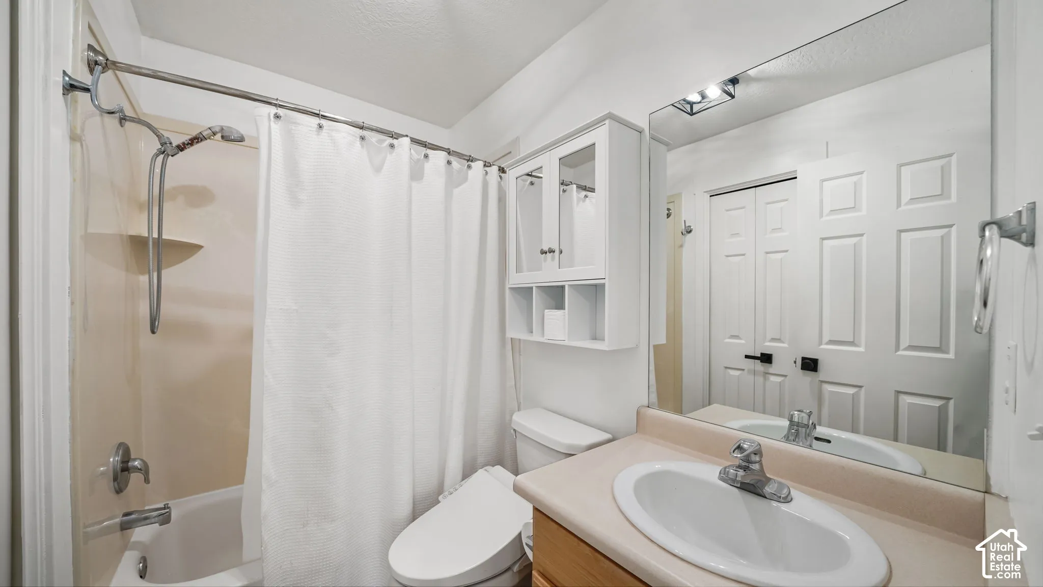 Bathroom featuring a built-in tub and shower combination, vanity with an integrated sink, wall-mounted mirror, and overhead storage cabinetry