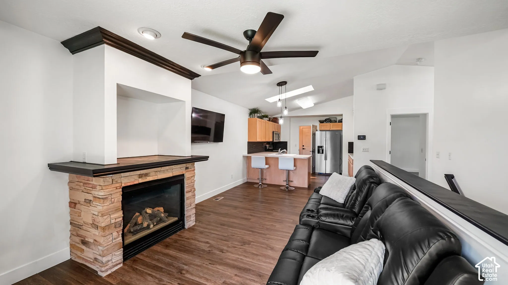 Stone-clad fireplace with mantel, dark wood-finish flooring, vaulted ceilings, and a ceiling fan