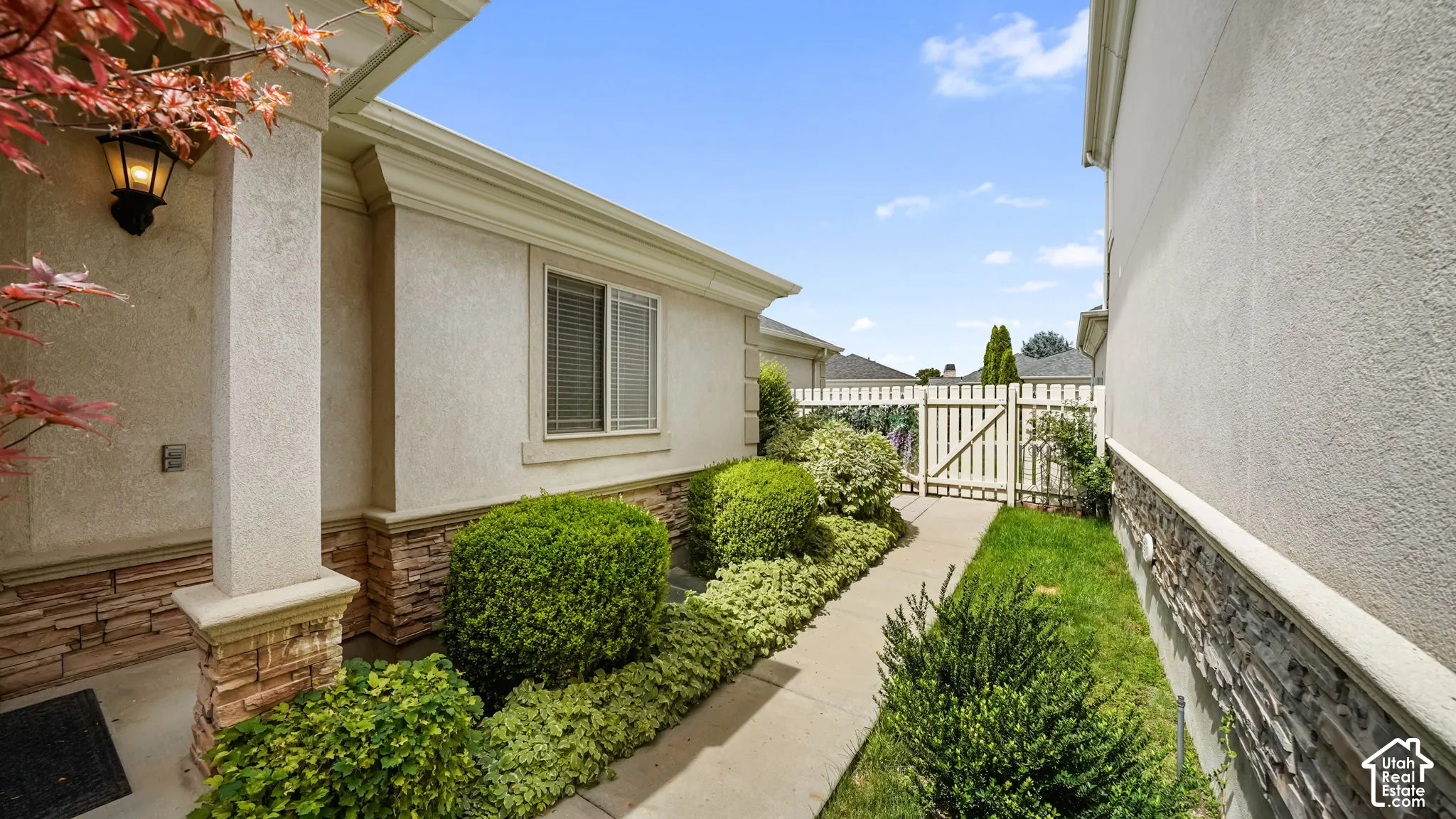 Stucco exterior with stone veneer accents, decorative sconce lighting, and a gated side yard
