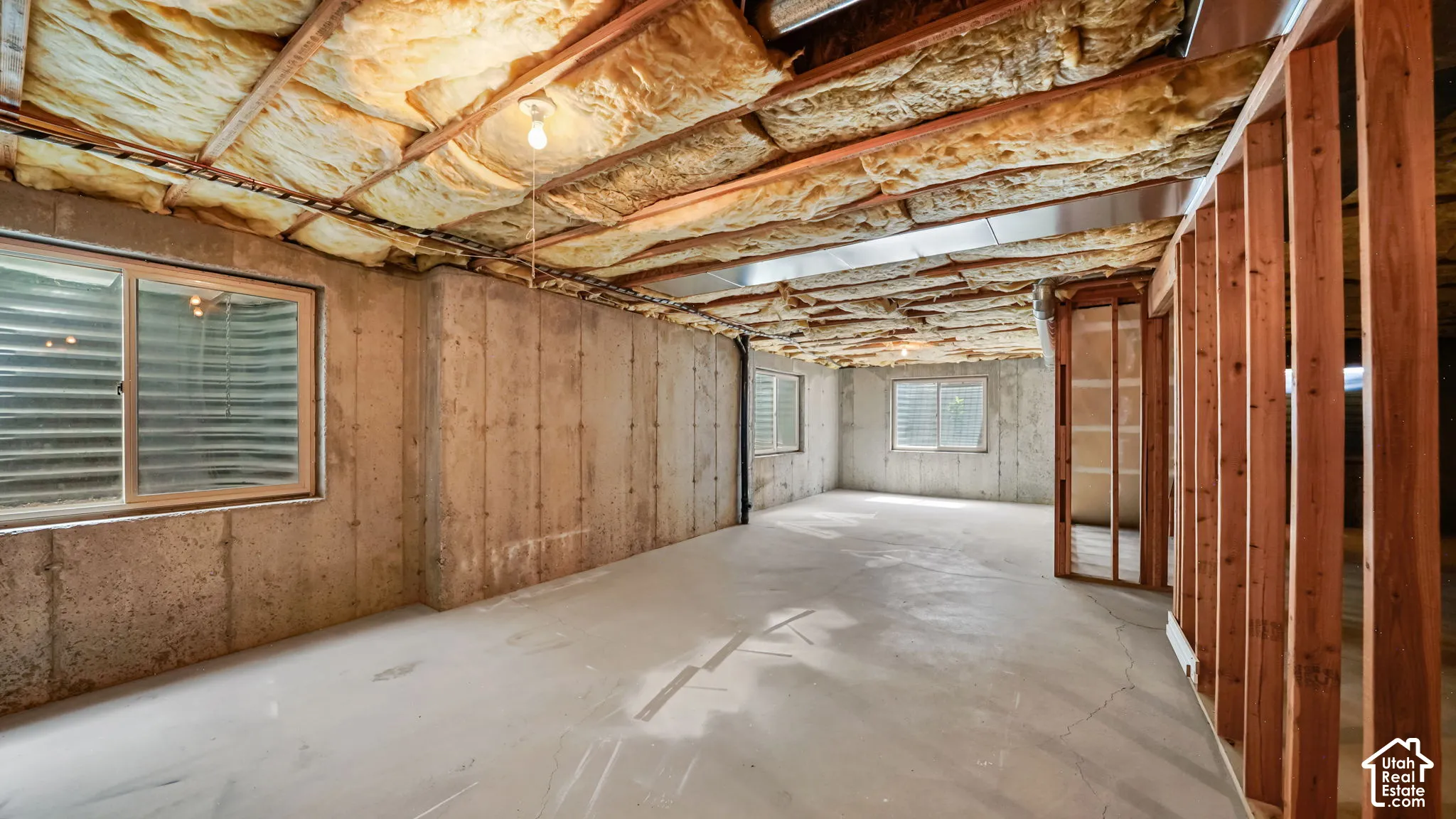 Unfinished basement space with concrete walls, exposed ceiling insulation, and structural framing