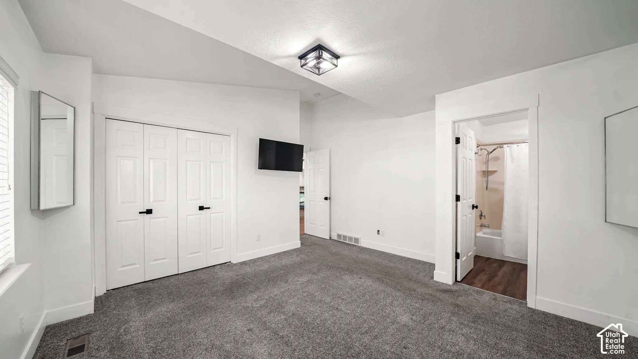 Neutral tone wall paint, vaulted ceiling, plush carpet flooring, bi-fold closet doors with matte black hardware, and an en-suite bathroom featuring wood-finish flooring and a shower-tub combination