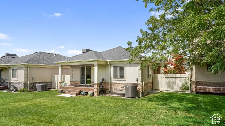 Expansive grass lawn with a covered patio featuring stone-clad pillars, sliding glass door access, and a wood-finish deck