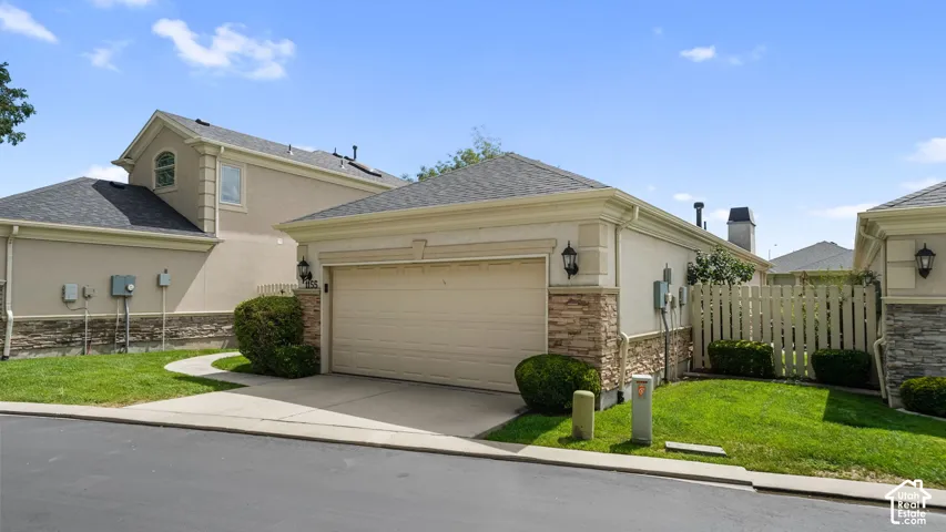 Two-car garage with overhead door, stone veneer accents, stucco exterior, and black asphalt shingle roof