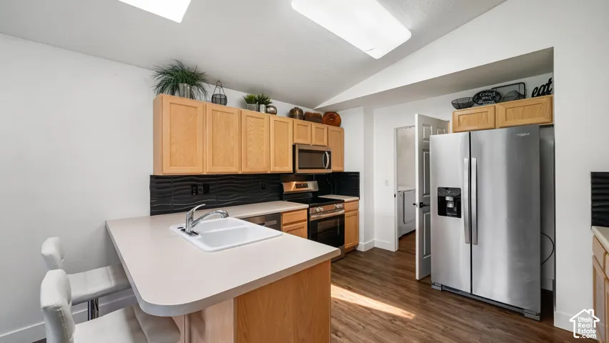 Kitchen featuring wood-finish cabinetry, stainless steel appliances, a breakfast bar, and a textured black backsplash