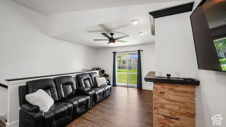 Lower-level living area featuring wood-finish flooring, a stone-clad fireplace with hearth, a ceiling fan, recessed lighting, and a sliding glass door leading to the exterior