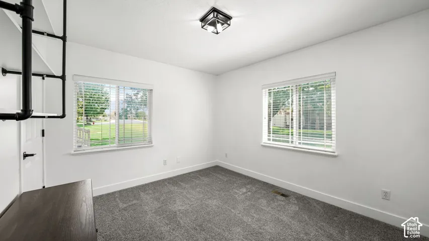 Recessed lighting, two windows with blinds, dark gray carpeting, and a built-in shelving unit
