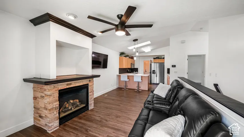 Stone-clad fireplace with mantel, dark wood-finish flooring, vaulted ceilings, and a ceiling fan