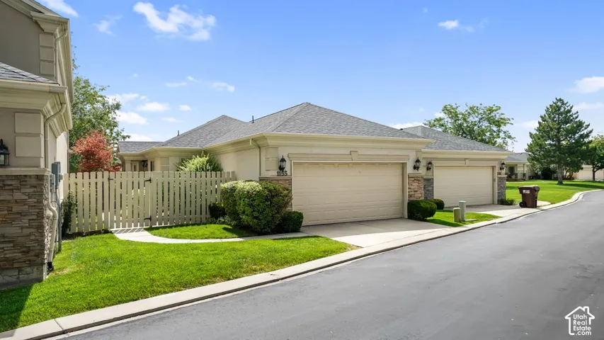 Stucco exterior with stone accents, attached garage, manicured landscaping, and a picket fence