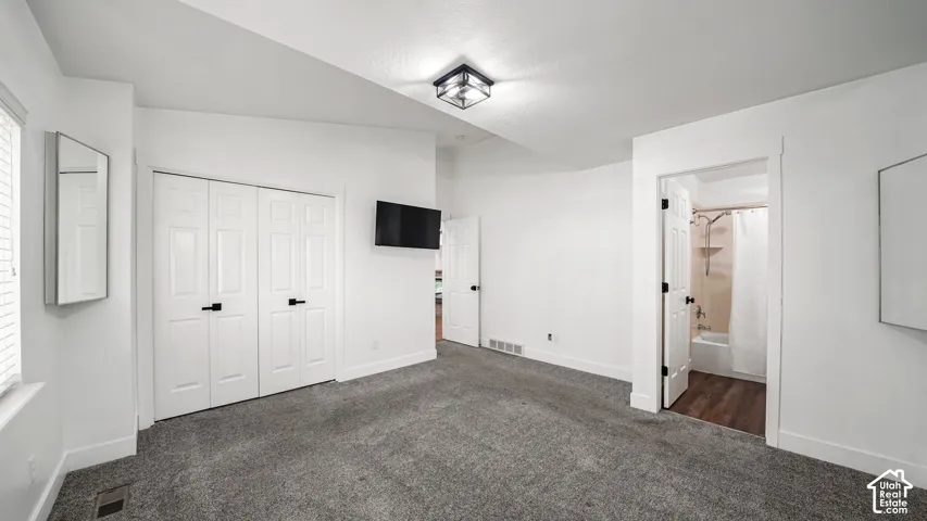 Neutral tone wall paint, vaulted ceiling, plush carpet flooring, bi-fold closet doors with matte black hardware, and an en-suite bathroom featuring wood-finish flooring and a shower-tub combination