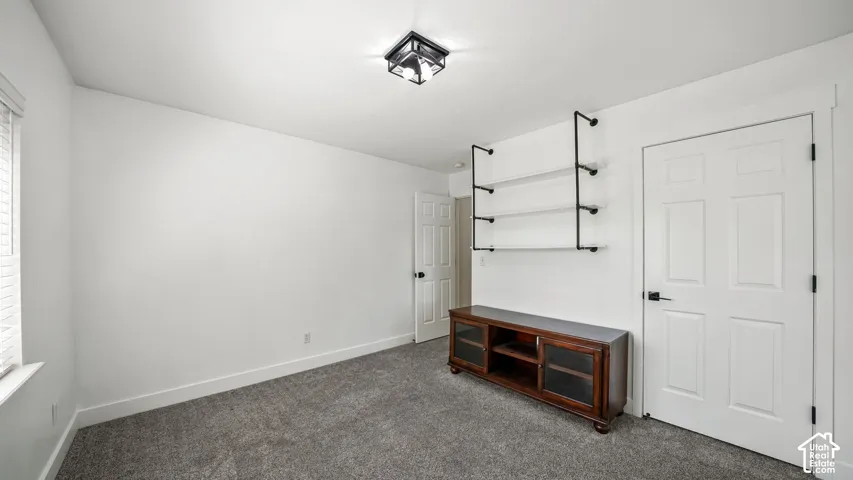 Recessed window with blinds, white walls, gray carpeting, wall-mounted shelving, and a flush mount light fixture