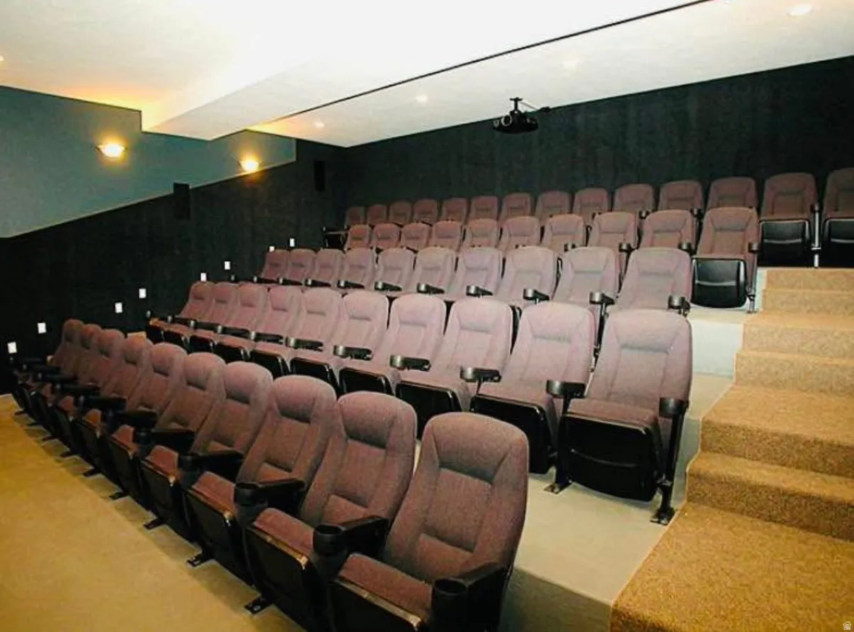 Dedicated theater room featuring tiered seating, wall-mounted sconces, and integrated step lighting