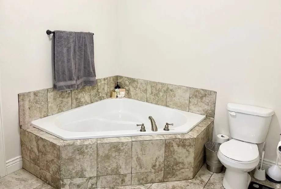Corner soaking tub with tiled surround, brushed nickel fixtures, and coordinating floor tiling