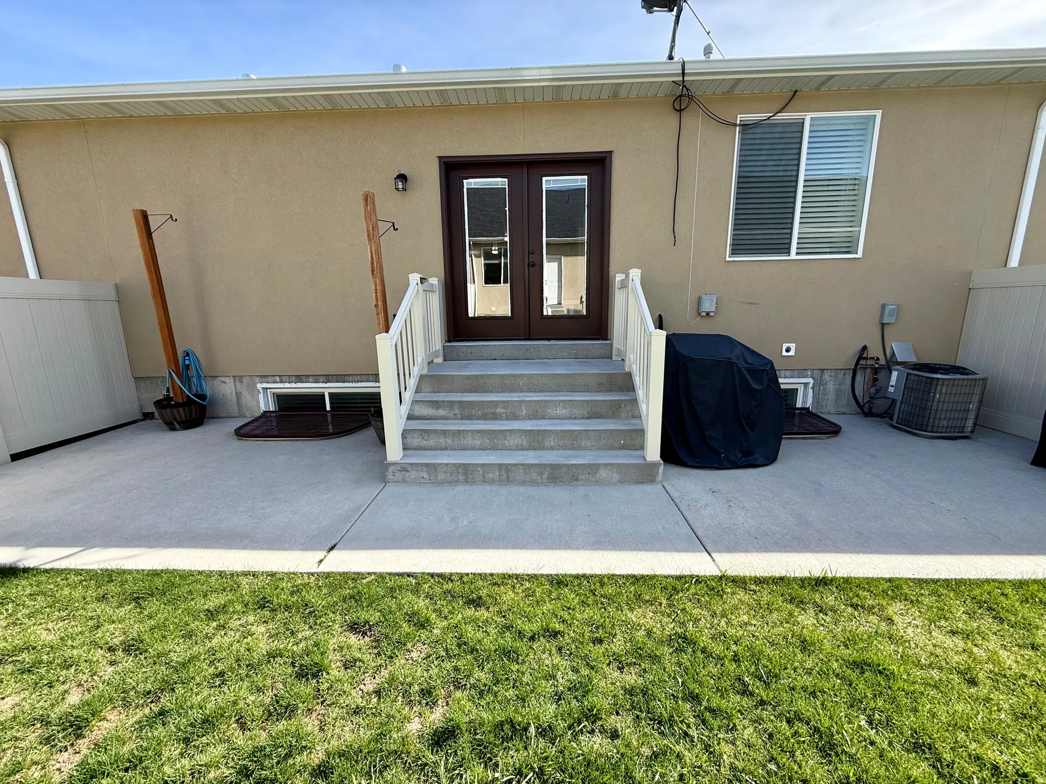 Expansive concrete patio with direct outdoor access via double doors, featuring a multi-step concrete staircase with white railings, and a manicured lawn area