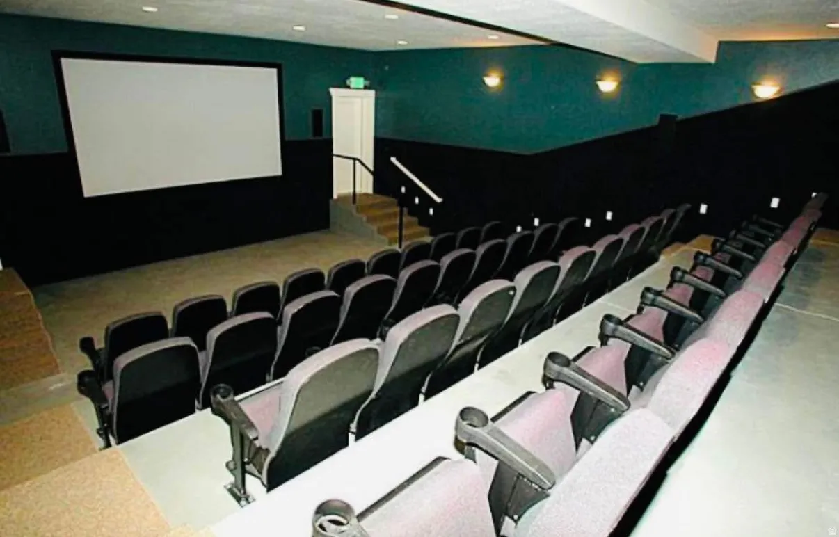 Dedicated screening room featuring tiered seating, a large projection screen, and wall sconce lighting