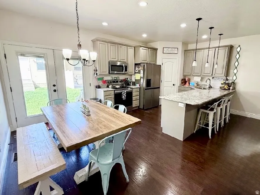 Wood-finish flooring throughout, kitchen island with seating, stainless steel appliances, pendant lighting, and double glass-paneled doors