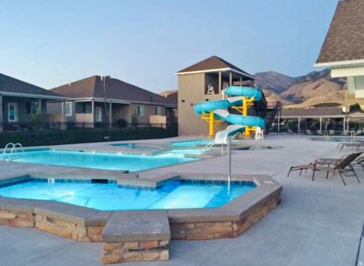 Community pool with integrated hot tub, multi-level water slide, structured pool house, and surrounding hardscape