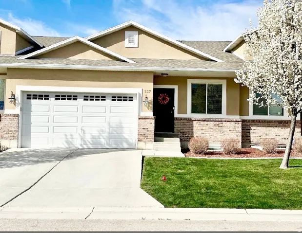 Two-story townhome featuring a neutral stucco and brick exterior, white garage door, and concrete driveway