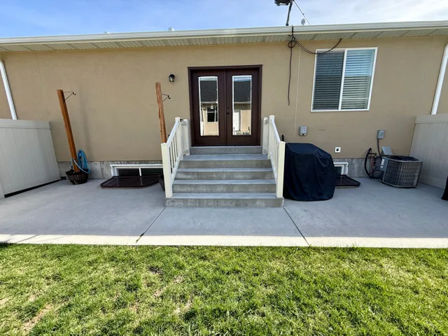 Expansive concrete patio with direct outdoor access via double doors, featuring a multi-step concrete staircase with white railings, and a manicured lawn area