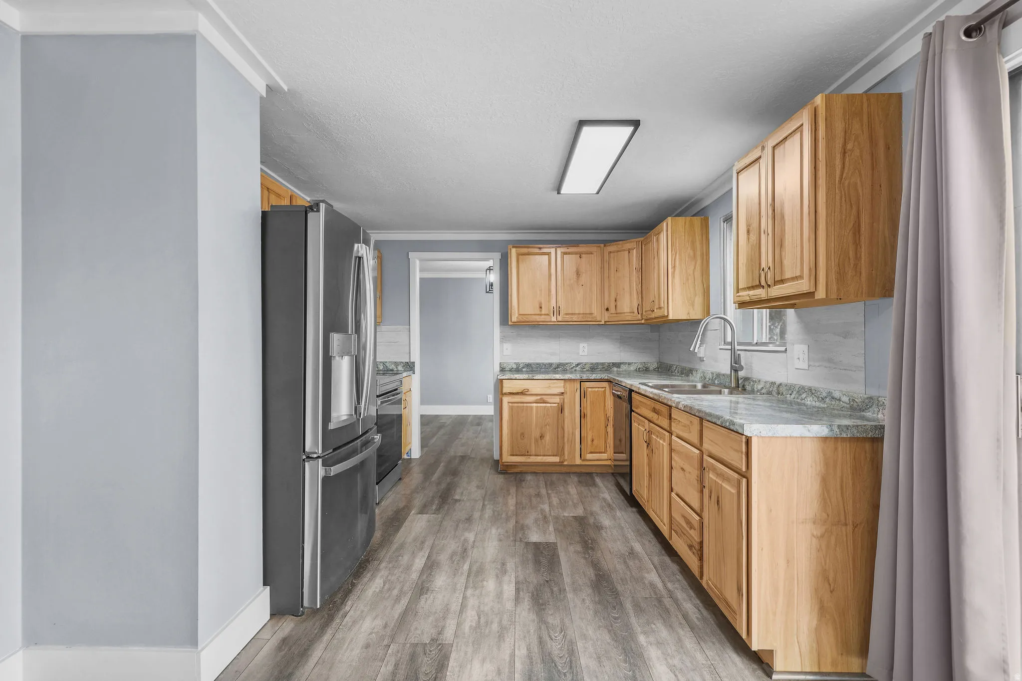 Kitchen featuring wood-finish cabinetry, light-toned countertops, stainless steel appliances, a tile backsplash, and wood-finish flooring