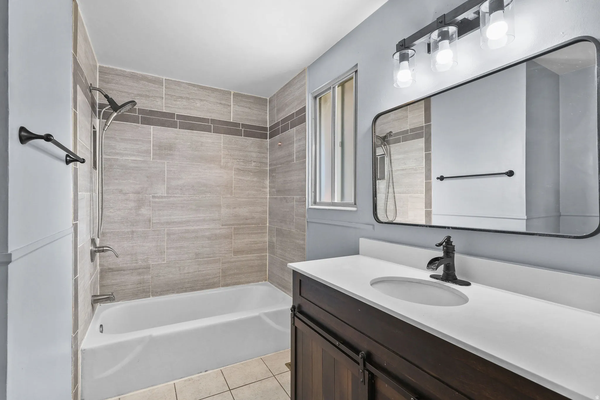 White bathtub with tile surround, dark wood-finish vanity with white countertop, and rectangular mirror