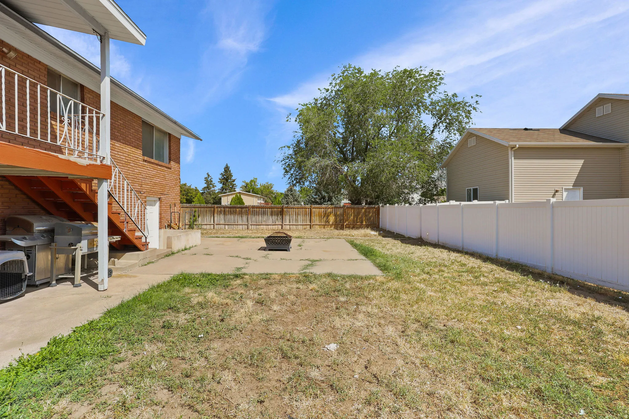 Brick exterior with an elevated deck, concrete patio, and a privacy fence