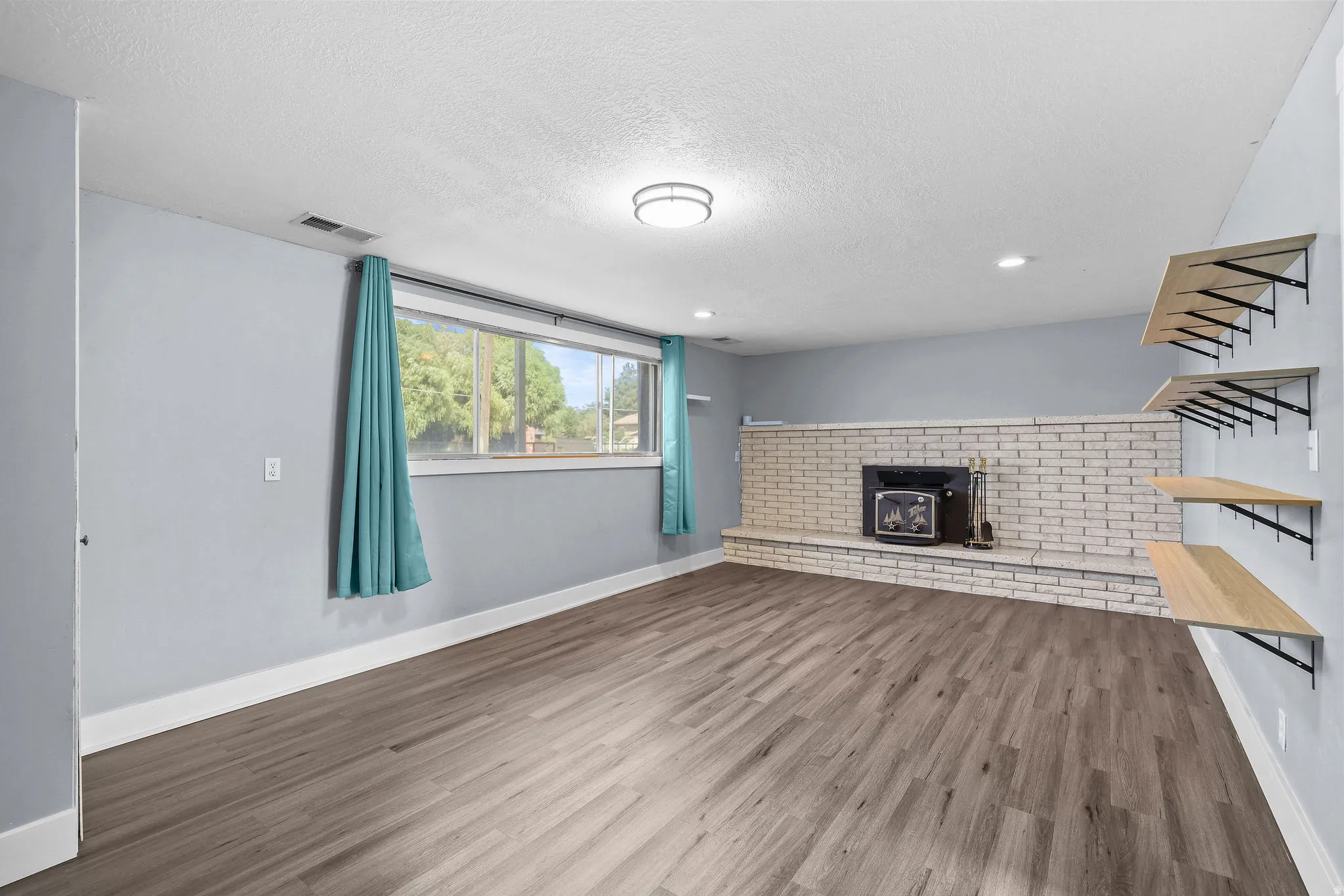 Spacious room featuring wood-finish flooring, a white brick fireplace, and built-in shelving