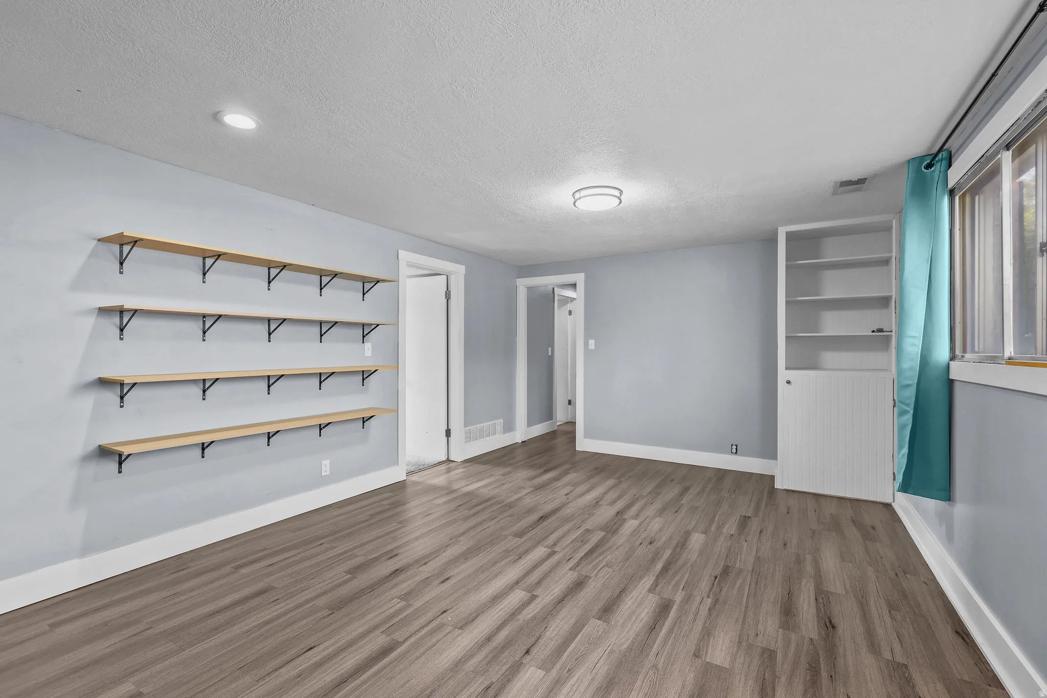 Wood-finish flooring, recessed lighting, and wall-mounted shelving in a spacious room