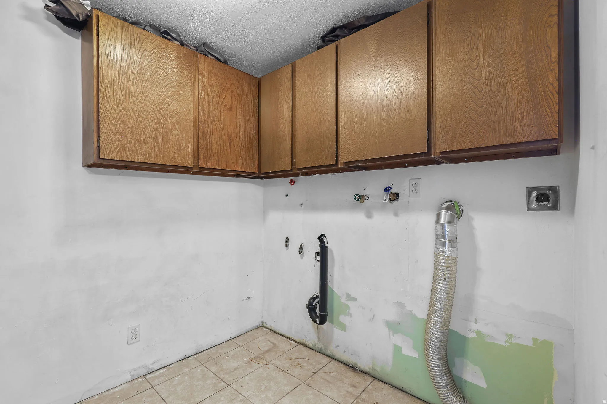 Overhead wood-finish cabinetry, tile flooring, and utility hookups