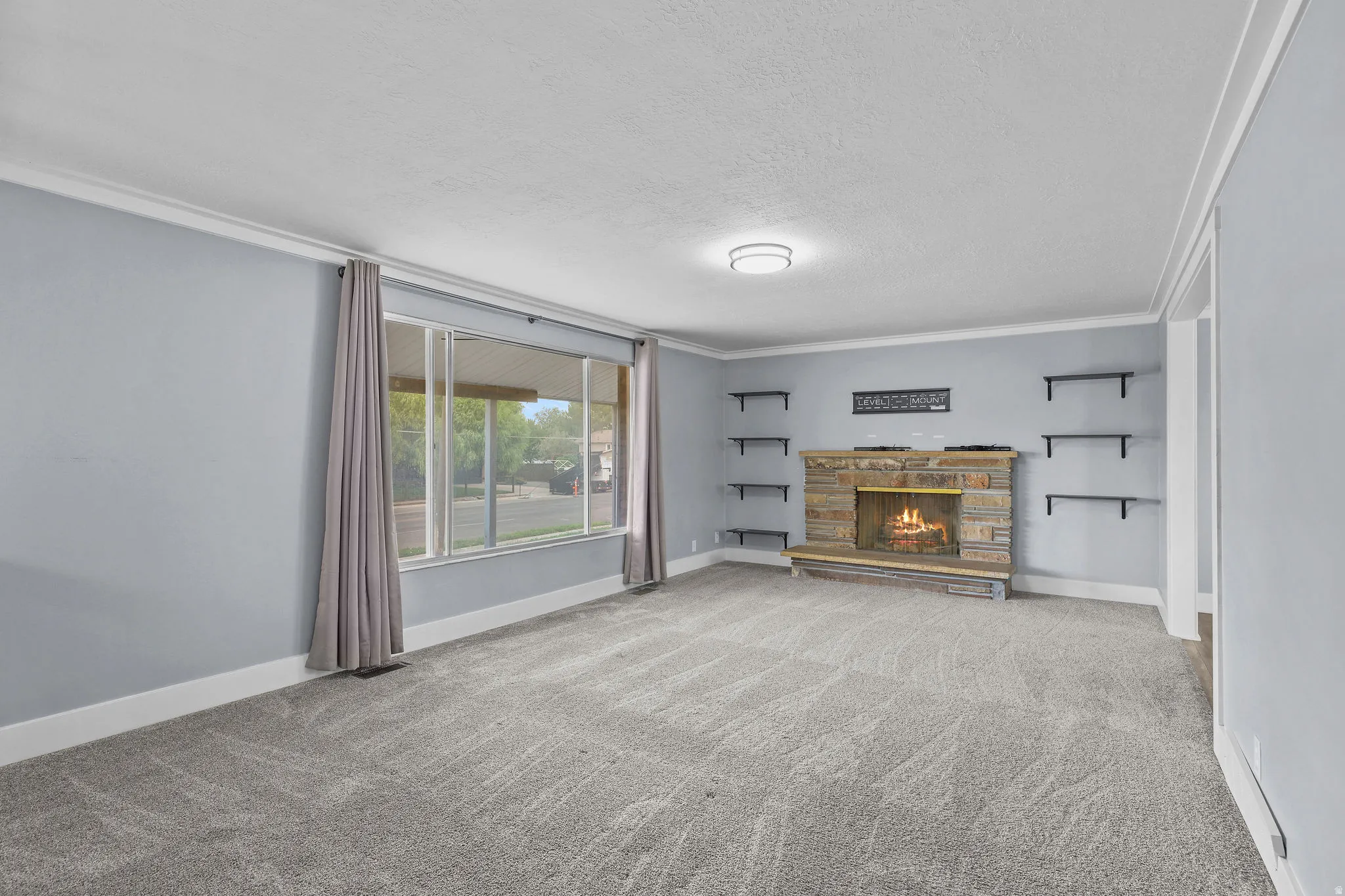 Expansive living area with grey carpeting, a stone fireplace, built-in shelving, and a large picture window
