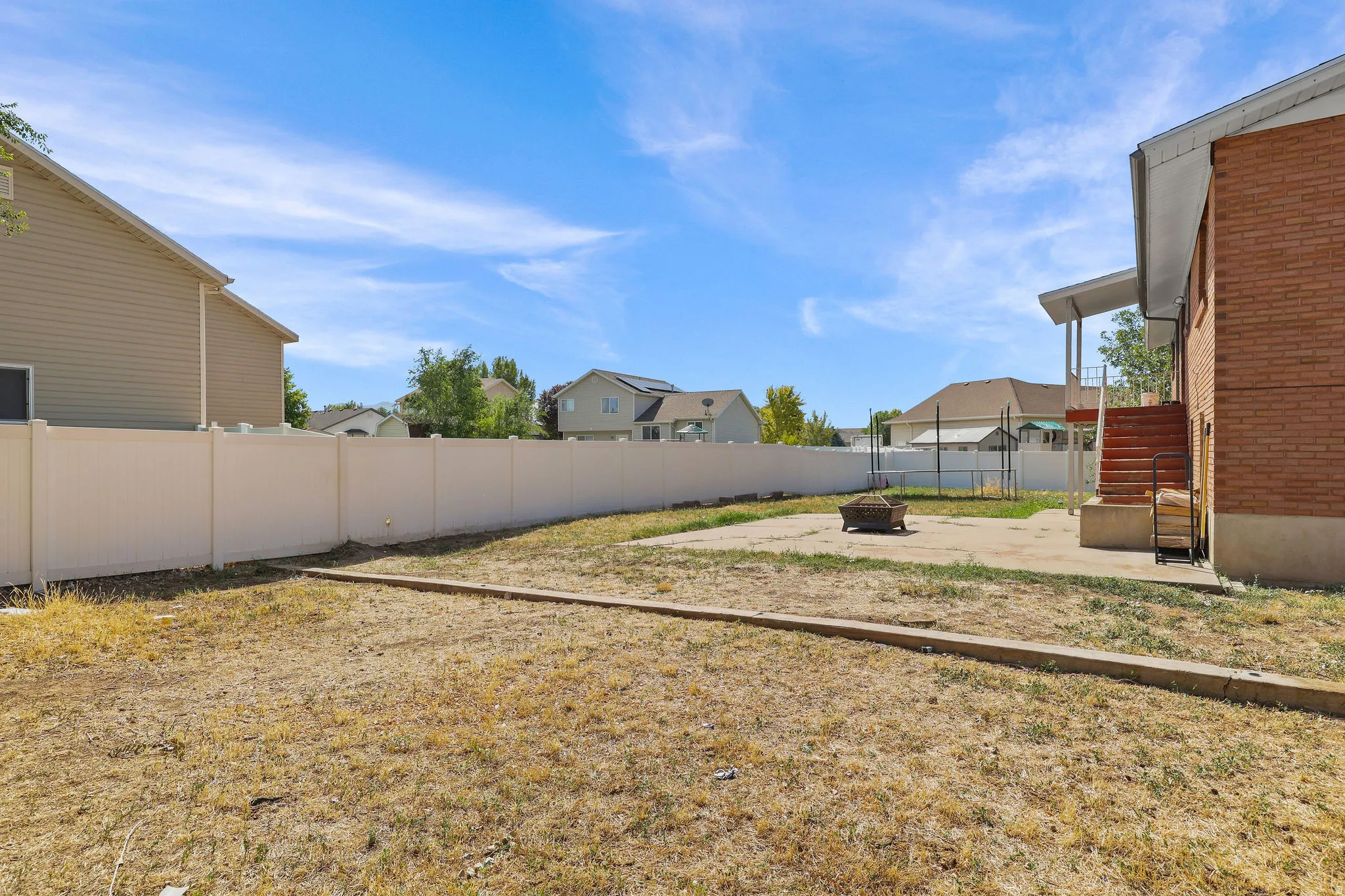Expansive backyard featuring a privacy fence, concrete patio, and a brick-clad exterior