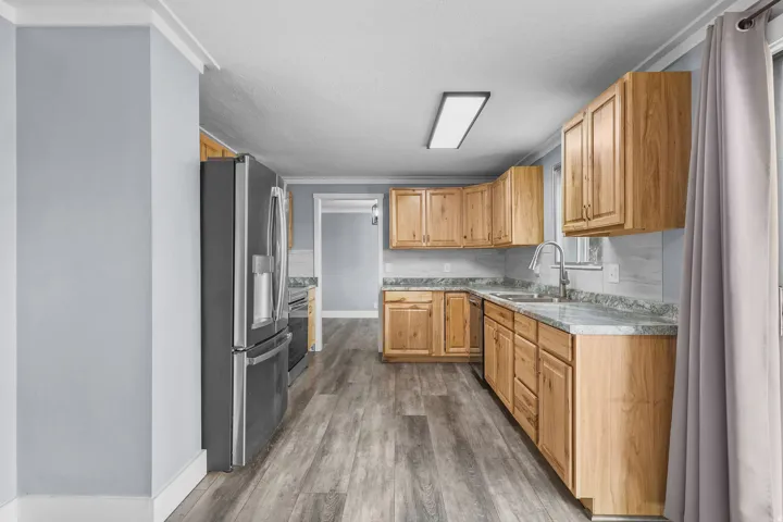 Kitchen featuring wood-finish cabinetry, light-toned countertops, stainless steel appliances, a tile backsplash, and wood-finish flooring