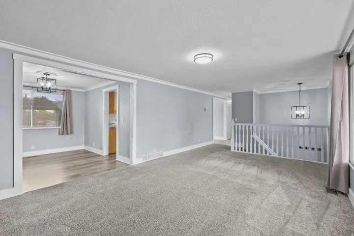 Spacious carpeted area with a white banister and open staircase