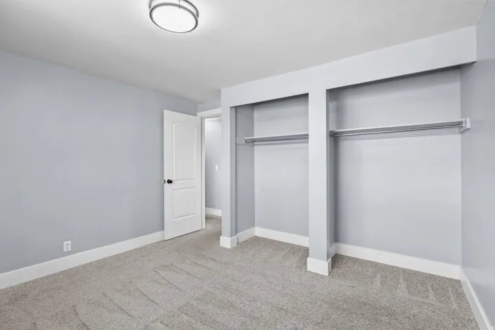 Plush carpet flooring, neutral wall tones, white trim, and a built-in closet with hanging rods