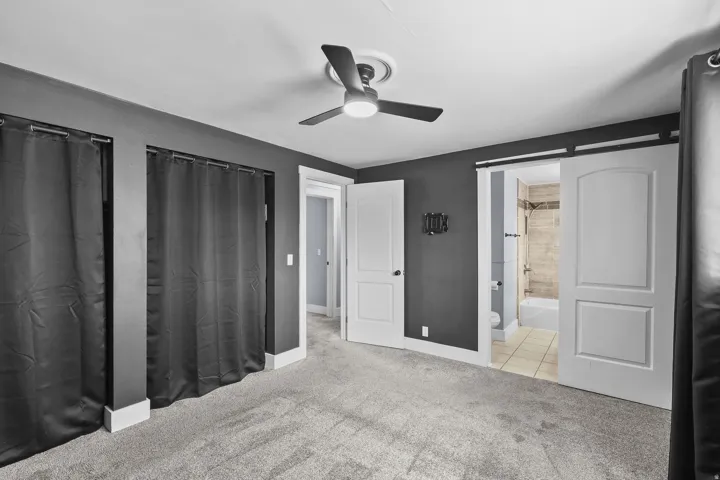 Ceiling fan with light kit, barn door entry, full bathroom with tiled shower surround, recessed lighting, and carpet flooring