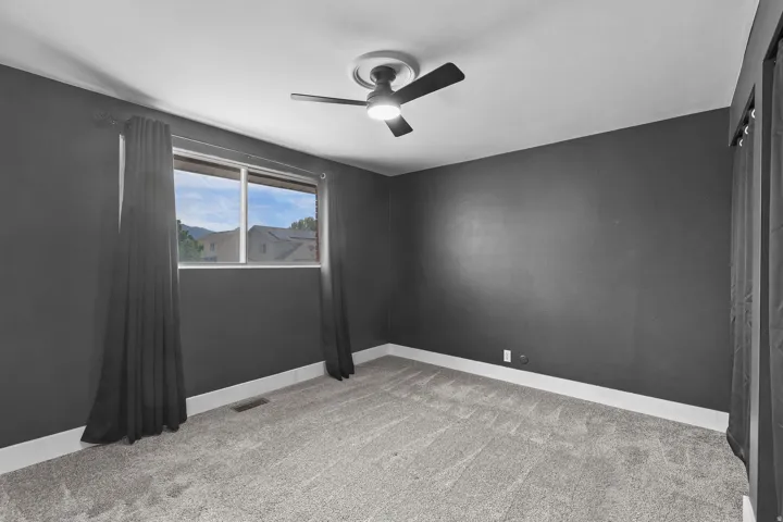 Neutral tone walls with an expansive window, gray carpet, and a ceiling fan with integrated lighting