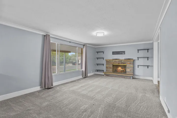 Expansive living area with grey carpeting, a stone fireplace, built-in shelving, and a large picture window