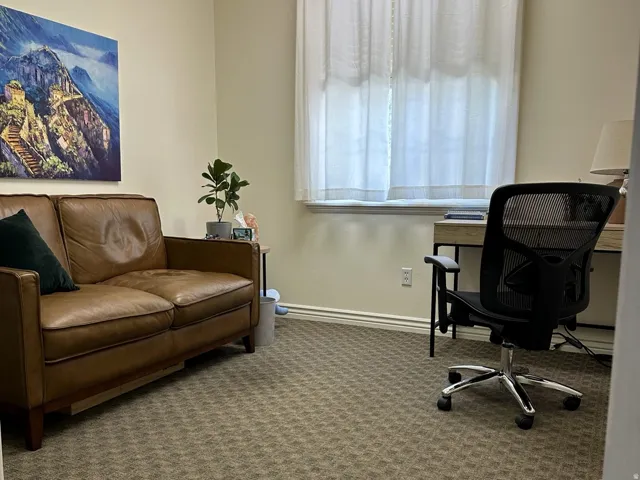 Wall-to-wall patterned carpeting, neutral wall color, and a window with sheer curtains