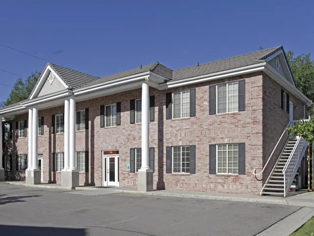 Two-story brick exterior with prominent white columns, dark shutters, and a grey tile roof