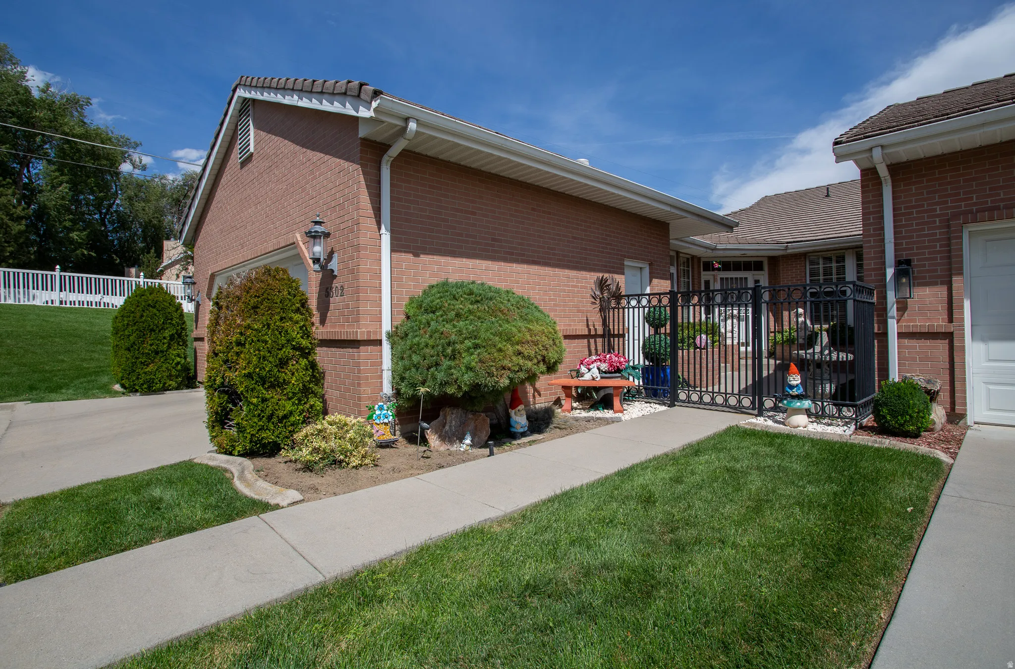 Brick exterior with white garage door, concrete driveway, and established shrubs