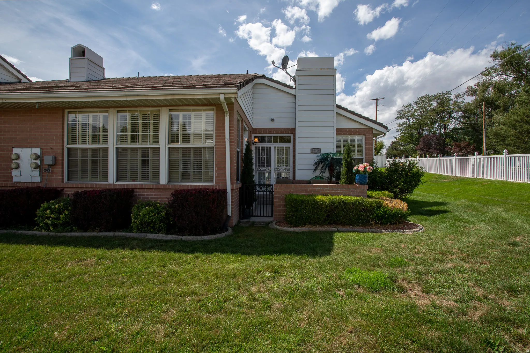 Brick exterior with white trim, multiple windows with blinds, an enclosed entry, and a white picket fence bordering the property