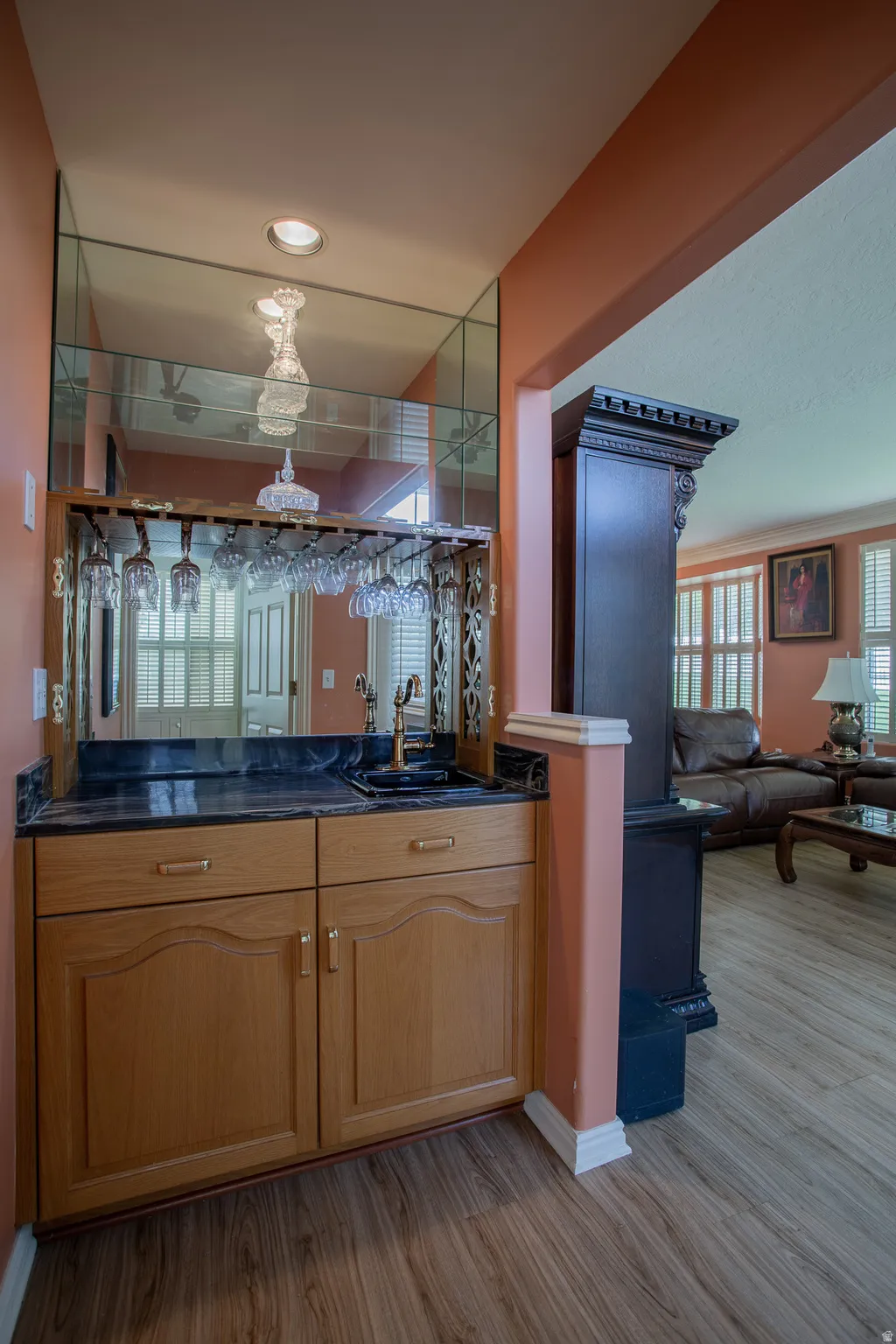 Built-in bar featuring wood cabinetry, a dark countertop, an integrated sink, and an overhead mirrored backsplash