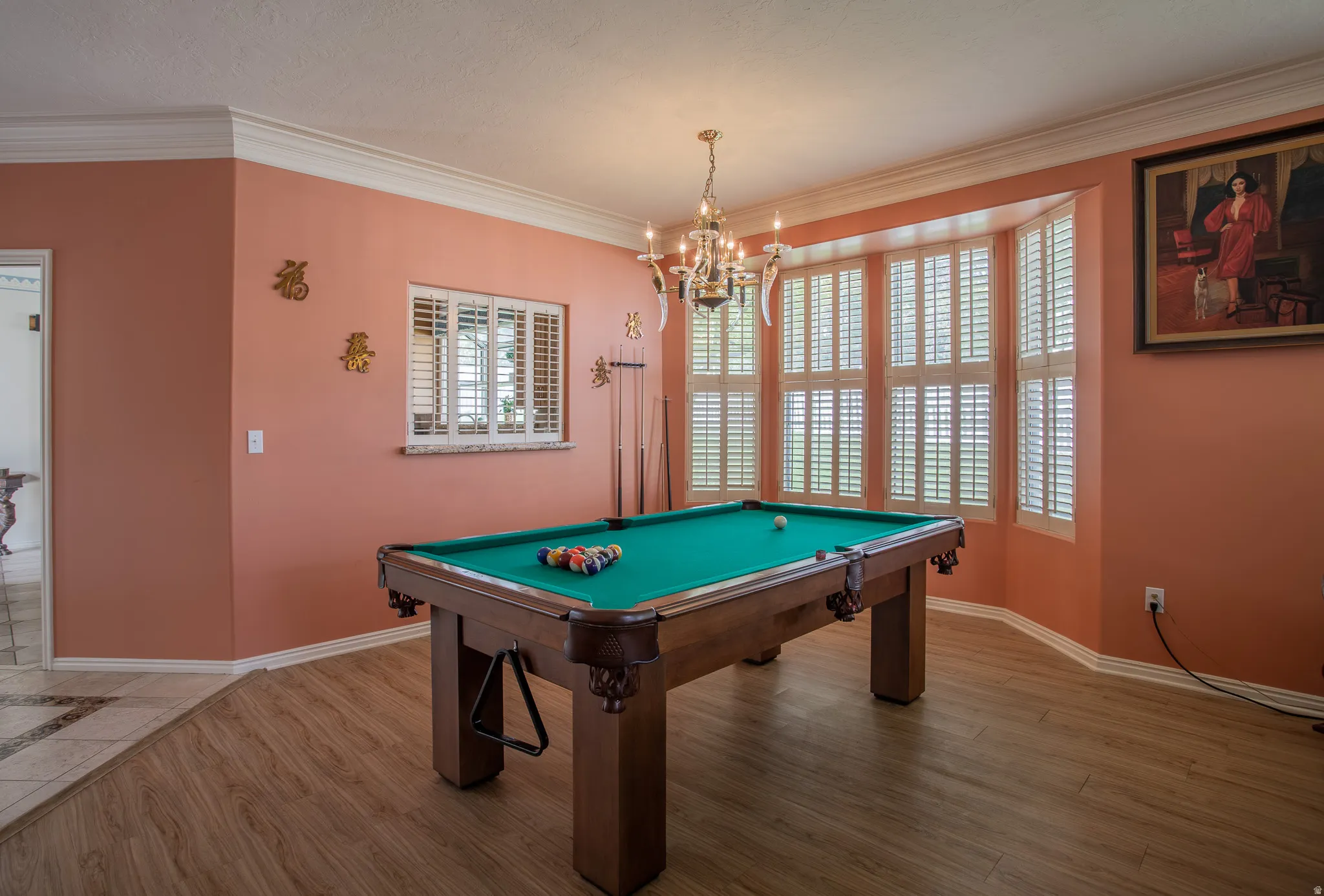 Wood-finish flooring, crown molding, and a bay window featuring plantation shutters