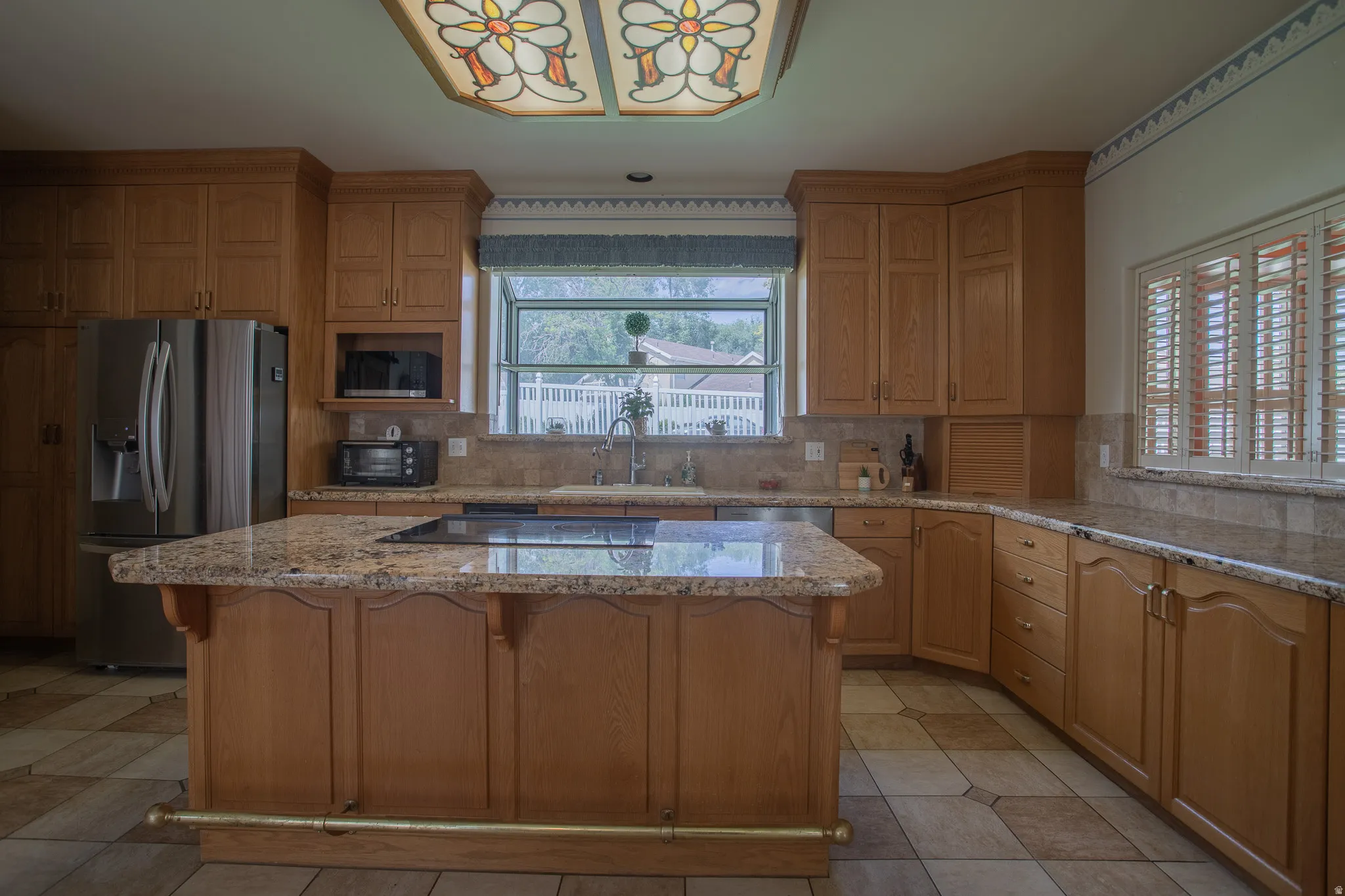 Expansive kitchen featuring an island with cooktop, granite countertops, wood cabinetry, stainless steel refrigerator, and tiled flooring
