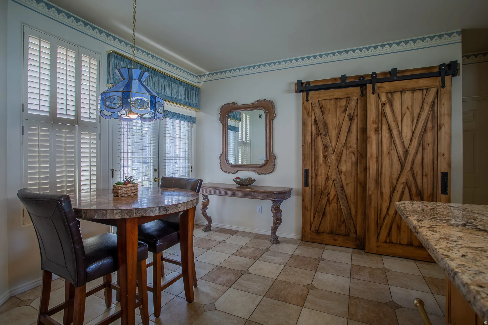 Wood-finish barn doors on a black iron track, patterned tile flooring, wood-framed mirror, and plantation shutters