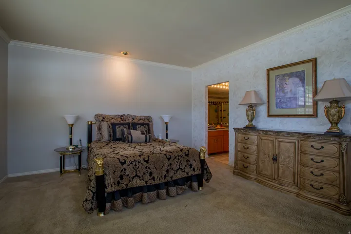 Carpeted flooring with crown molding, textured accent wall, recessed lighting, and a doorway to an additional space with a vanity