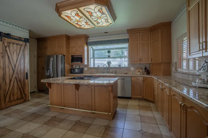 Wood-finish cabinetry with stone countertops, stainless steel appliances, a center island with cooktop, and a decorative ceiling fixture